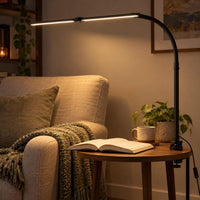 Zwarte klemlamp met warm licht boven een bijzettafeltje naast een fauteuil met open boek 1