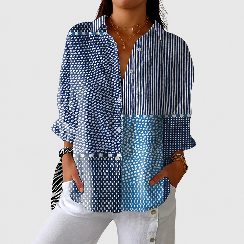 Vrouw draagt de blouse met blauwe stippen- en streepblokken, losjes gedragen met witte broek en handen in de zakken 1