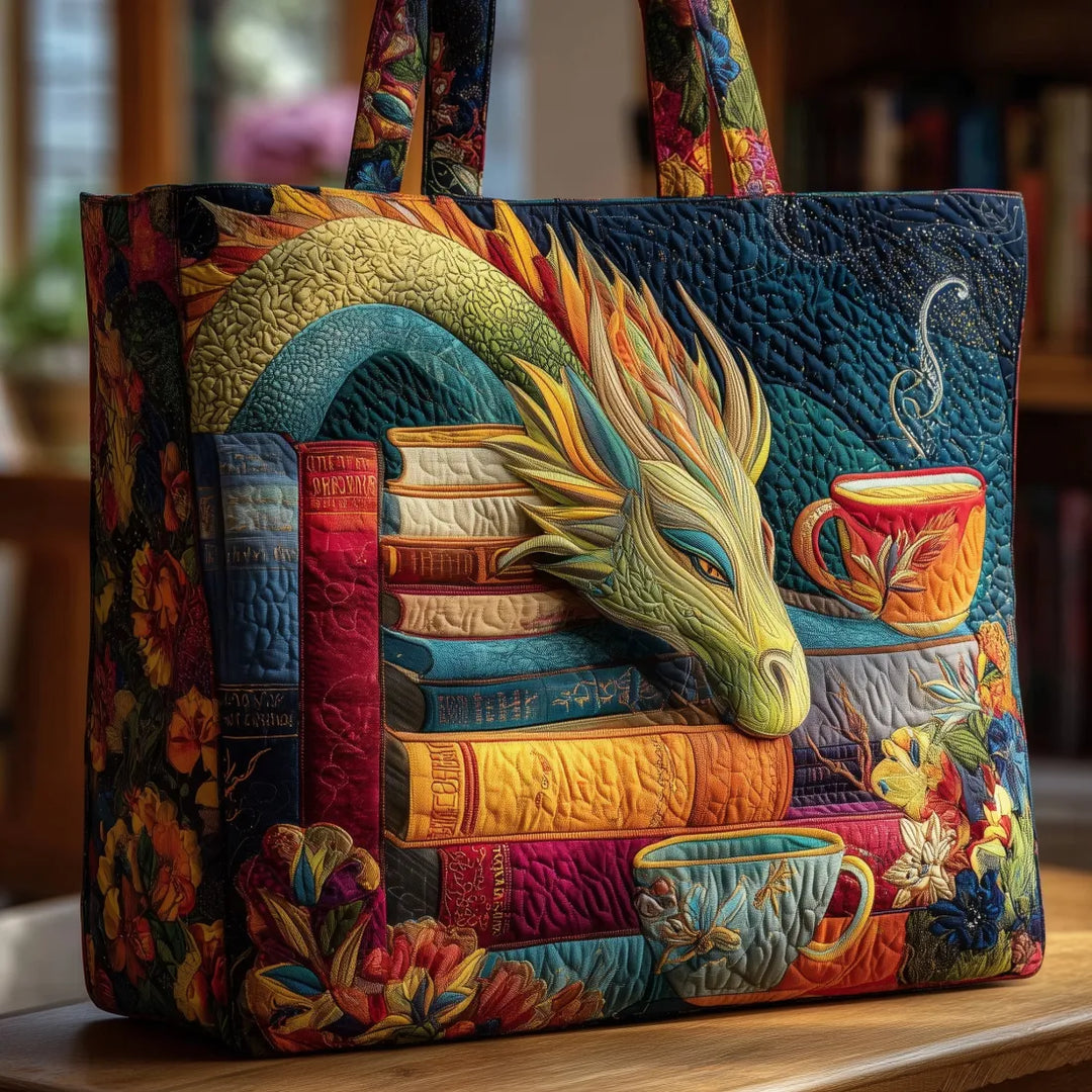 Gewatteerde totebag op een houten tafel, met een gestikte draak op een stapel kleurrijke boeken naast twee theekopjes en bloemen. 1