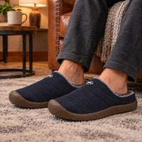 Donkerblauwe gewatteerde pantoffels met pluizige voering, gedragen op een beige tapijt bij een leren stoel 3