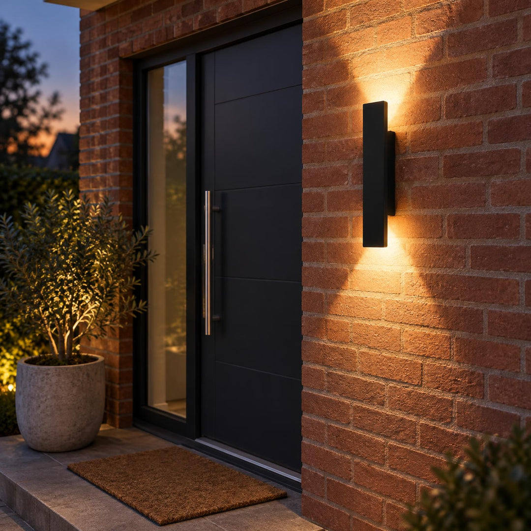 Zwarte wandlamp naast een zwarte voordeur op een bakstenen gevel, 's avonds met licht omhoog en omlaag 1