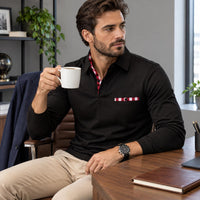 Man in zwarte poloshirt met rood geruite borstzak, zittend aan een bureau met koffiemok 1