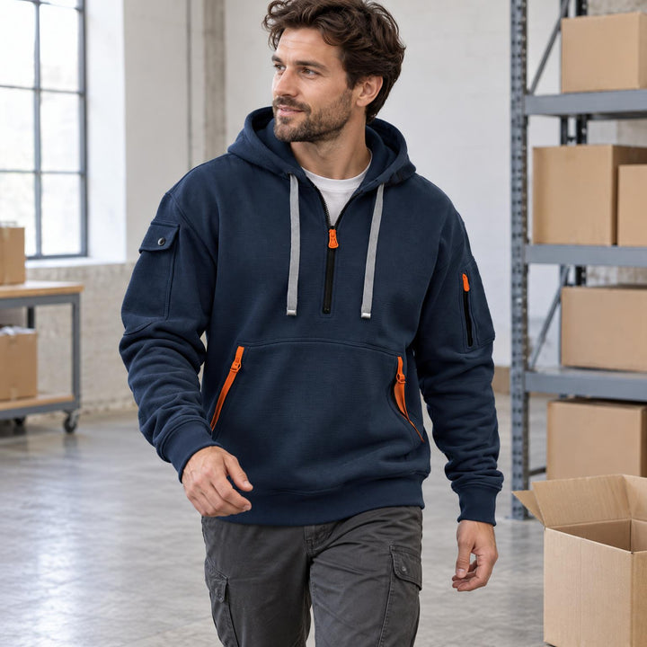 Marineblauwe hoodie met halve rits en oranje details, plat neergelegd op een betonnen vloer naast kartonnen dozen 1