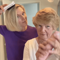 Vrouw in paars shirt borstelt haar blonde bob met een witte stylingborstel naast een oudere vrouw met kort haar. 9