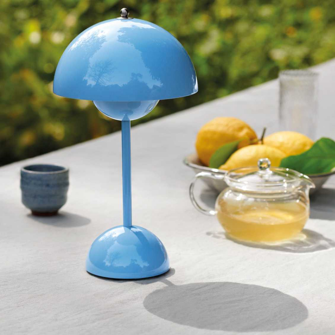 Glanzend lichtblauwe tafellamp op een buitentafel naast een glazen theepot, citroenen en een kopje 13