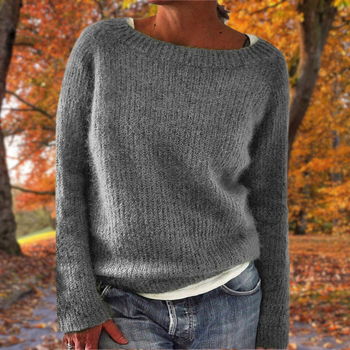 Vrouw draagt de gebreide trui in grijs over een wit shirt en spijkerbroek, in een herfstachtige omgeving. 4