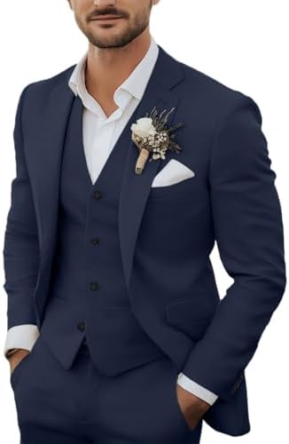 Model draagt het driedelige pak in marineblauw met wit overhemd, corsage en pochet, handen in de broekzakken. 1