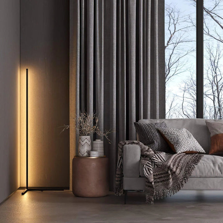 Verticale lamp met warm wit licht tegen een houten wand naast een grijze bank en hoge ramen 3