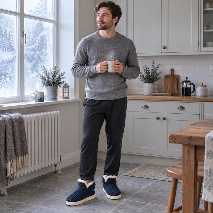 Man in grijze trui en donkere joggingbroek draagt blauwe hoge sloffen in een winterse keuken 1
