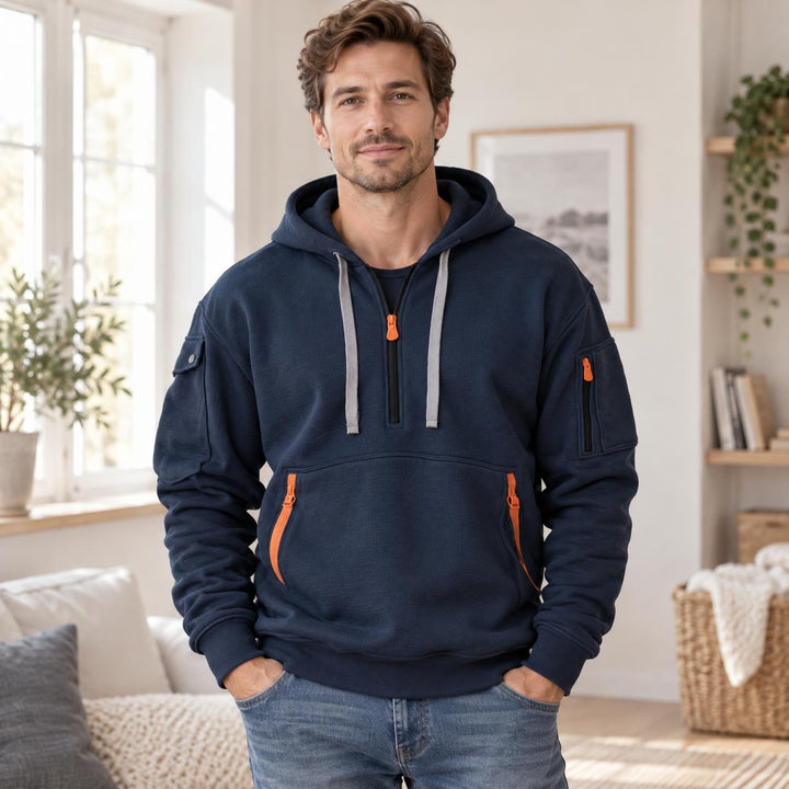 Man draagt de marineblauwe hoodie met halve rits en oranje ritstrekkers in een lichte woonkamer 1