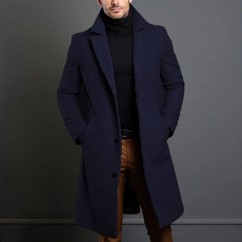 Lange overjas in donkerblauw gedragen door een model met zwarte coltrui en bruine broek, handen in de zakken. 4
