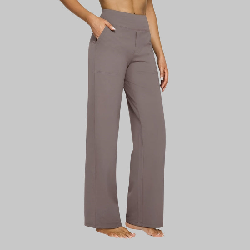 Model in taupebruine broek met hoge taille en rechte pijpen, zijaanzicht met een hand in de zakelijke zijzak. 1