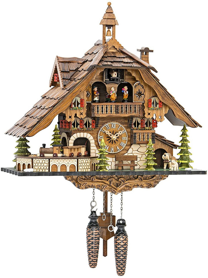 Houten koekoeksklok als chalet met belltoren, miniatuurtreintje, dennenbomen, hondjes en twee dennenappelgewichten, vrijstaand op een witte achtergrond. 1