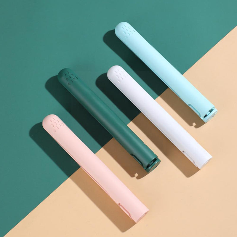 Vier gesloten stijltangen in blauw, donkergroen, wit en roze, schuin naast elkaar op een groen en beige vlak. 5