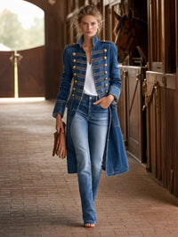 Model loopt in de blauwe denimjas met gouden knopen door een paardenstal, met jeans en leren handschoenen in de hand. 2