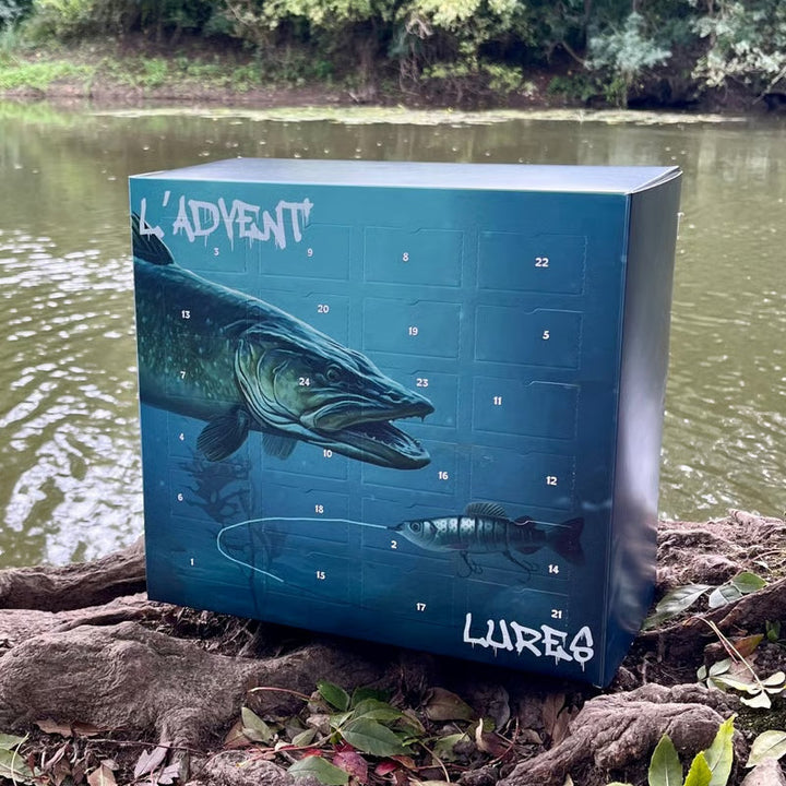 Blauwe kartonnen aftelkalender met snoek en kunstaasje, buiten op boomwortels voor een rivier 1