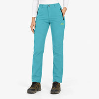 Vrouw draagt de softshellbroek in turquoise met wandelschoenen, voorkant met ritszakken en hand in zak 22