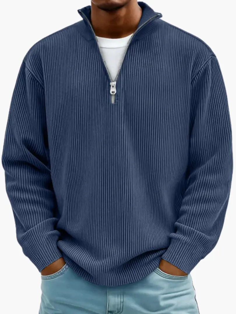 Model in de geribbelde trui met kwartrits in donkerblauw, met wit shirt eronder en handen in de zakken van de spijkerbroek. 5