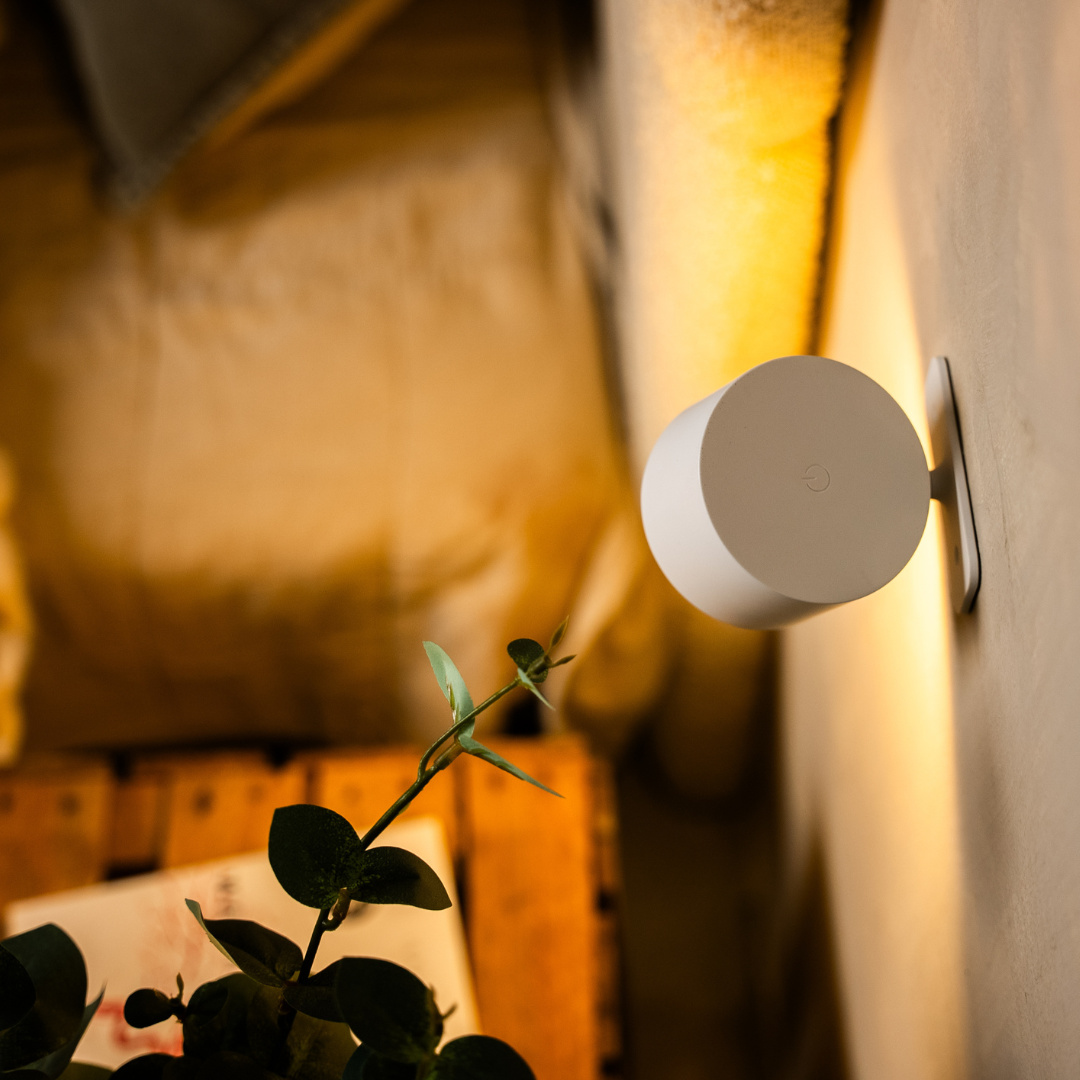 Achterkant van de witte wandlamp van opzij gezien, met een aanraakknop op de ronde achterplaat en de wandbevestiging. 13