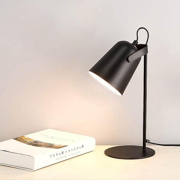 Zwarte versie van de bureaulamp met brandende kap, op een lichte tafel naast een opgeslagen boek. 12