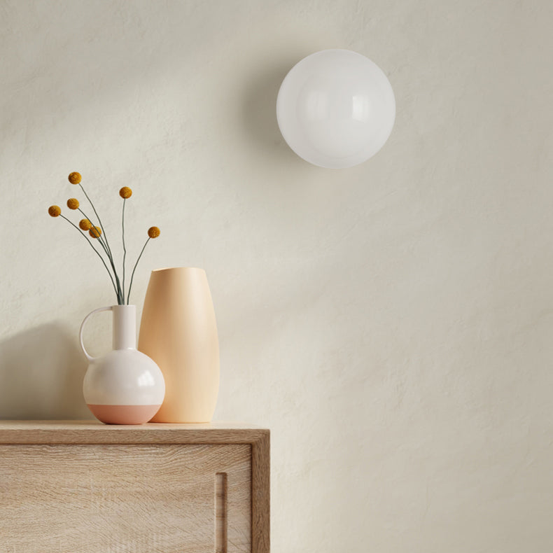 Uitgeschakelde witte glazen bol aan de muur boven een houten dressoir met vazen en droogbloemen 6