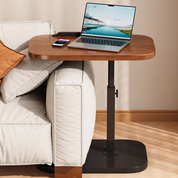Laptoptafel met het blad over de armleuning van een bank geschoven en de zwarte voet eronder, met laptop en telefoon erop. 11