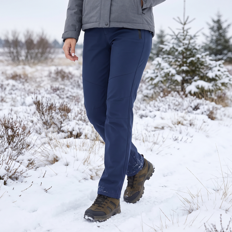 Vrouw wandelt in de sneeuw over de heide in marineblauwe softshellbroek en wandelschoenen 1