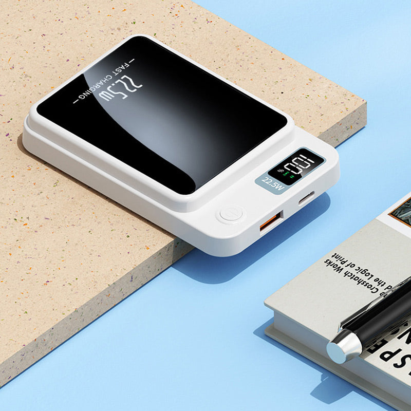 Witte powerbank liggend op een werkblad, met USB-A- en USB-C-poort, aan-knop en display zichtbaar, naast een boek en pen. 6