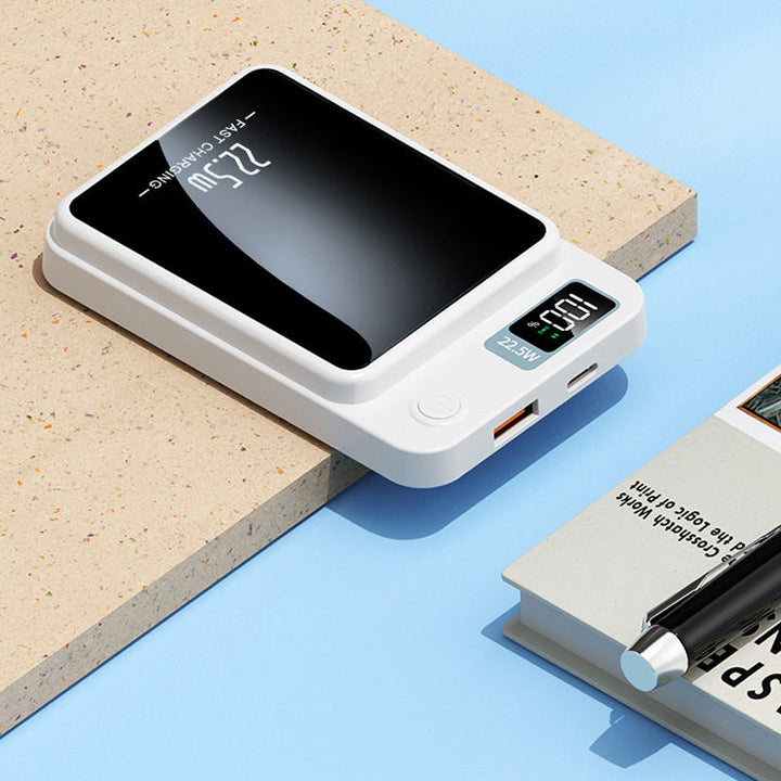 Witte powerbank liggend op een werkblad, met USB-A- en USB-C-poort, aan-knop en display zichtbaar, naast een boek en pen. 6