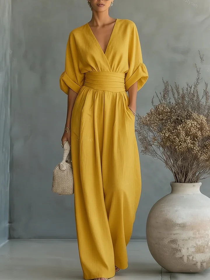 Dezelfde jumpsuit in mosterdgeel, van voren gedragen met de hand in de zak, voor een grijze achtergrond. 3