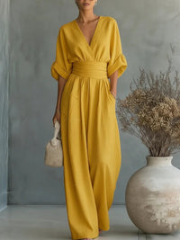Dezelfde jumpsuit in mosterdgeel, van voren gedragen met de hand in de zak, voor een grijze achtergrond. 3