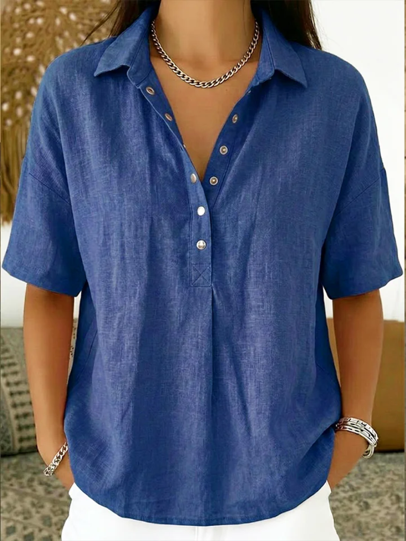 Model draagt de blouse in blauw met korte mouwen, diepe knoopsluiting en zilverkleurige ketting 1