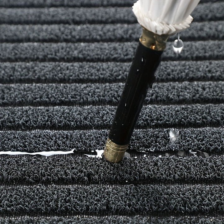 Close-up van de grijze lussenstructuur van de mat, waarop een paraplu staat met water en druppels ertussen. 3