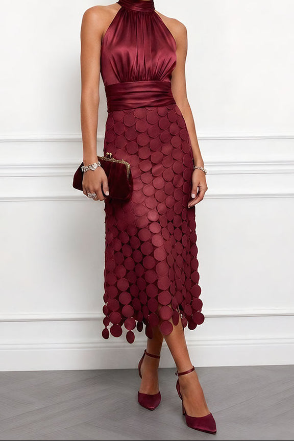 Model draagt de halsjurk in bordeauxrood met een kleine clutch met gouden sluiting en rode pumps, rok met schijfjes. 5