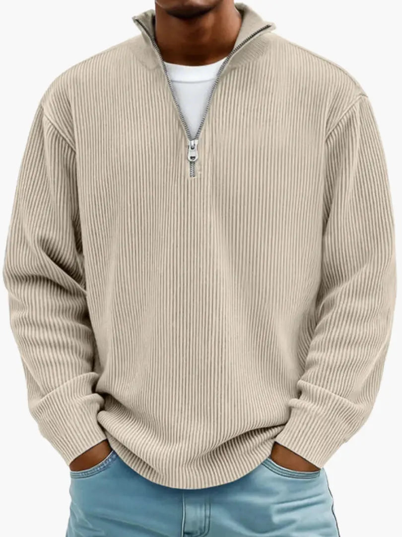 De geribbelde trui met ritskraag in beige, gedragen door een model over een wit shirt en met een lichtblauwe spijkerbroek. 4