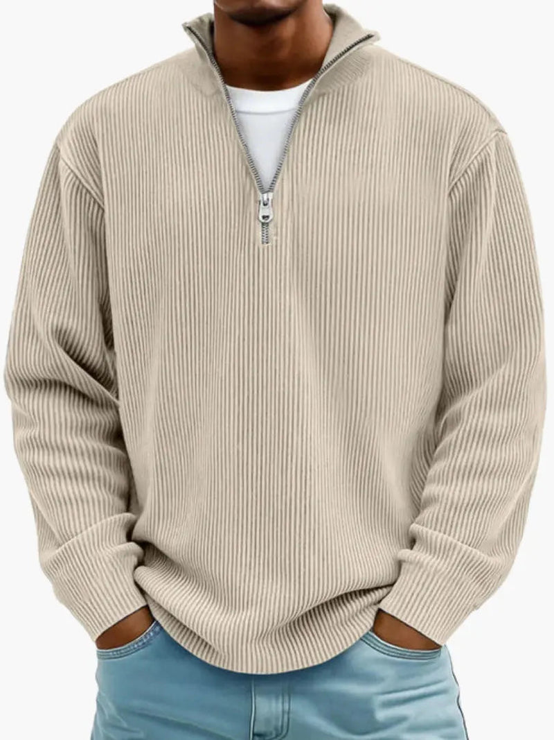 De geribbelde trui met ritskraag in beige, gedragen door een model over een wit shirt en met een lichtblauwe spijkerbroek. 4
