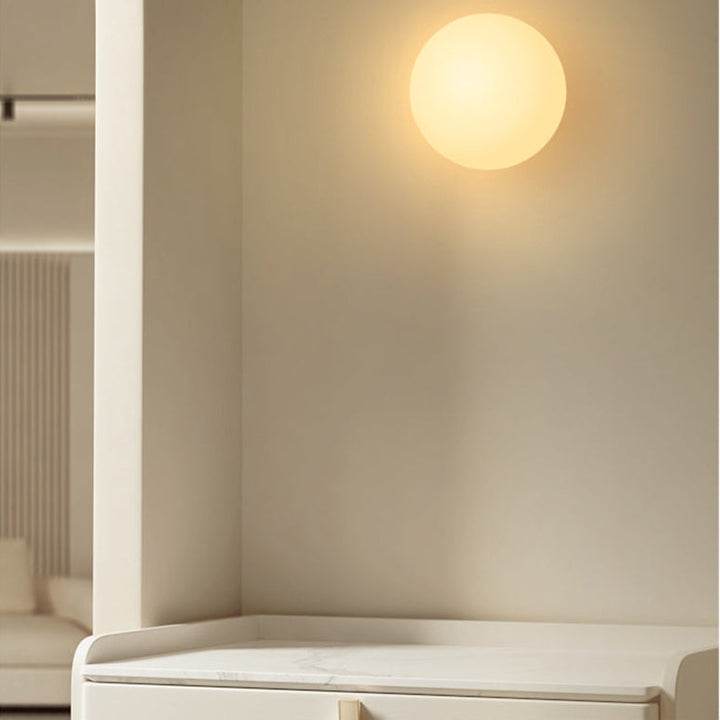 Opaalglazen bol als wandlamp boven een crèmekleurig dressoir met marmeren blad in warm licht 3