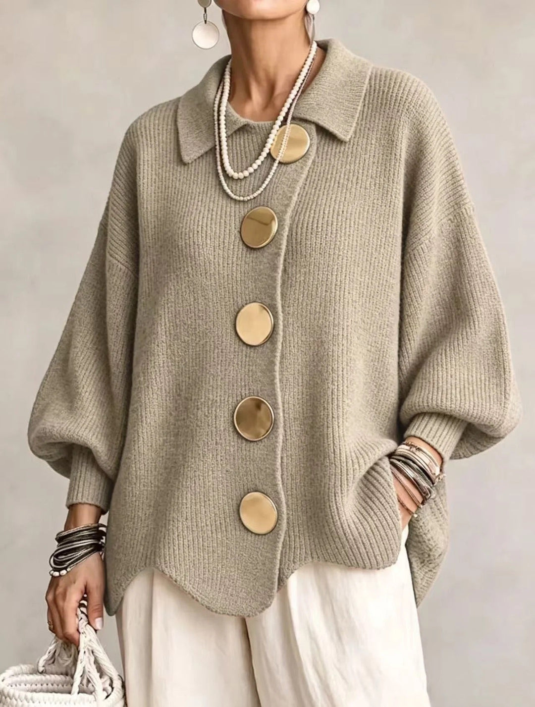 Model draagt het gebreide vest in groenig beige met gouden knopen en een witte broek, vooraanzicht. 17