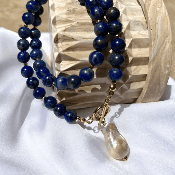 Dubbele rij blauwe kralen met parelhanger en sluiting op witte stof naast een houten object 9