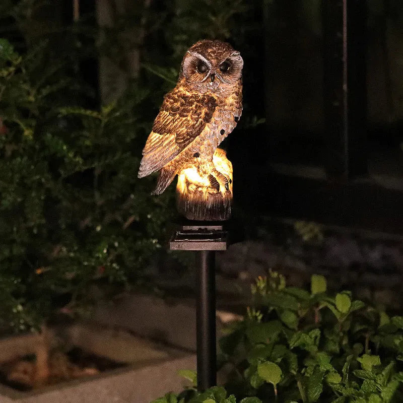 Bruine uil op boomstronk geeft 's nachts warm licht in een donkere tuin, met groene planten op de voorgrond. 4