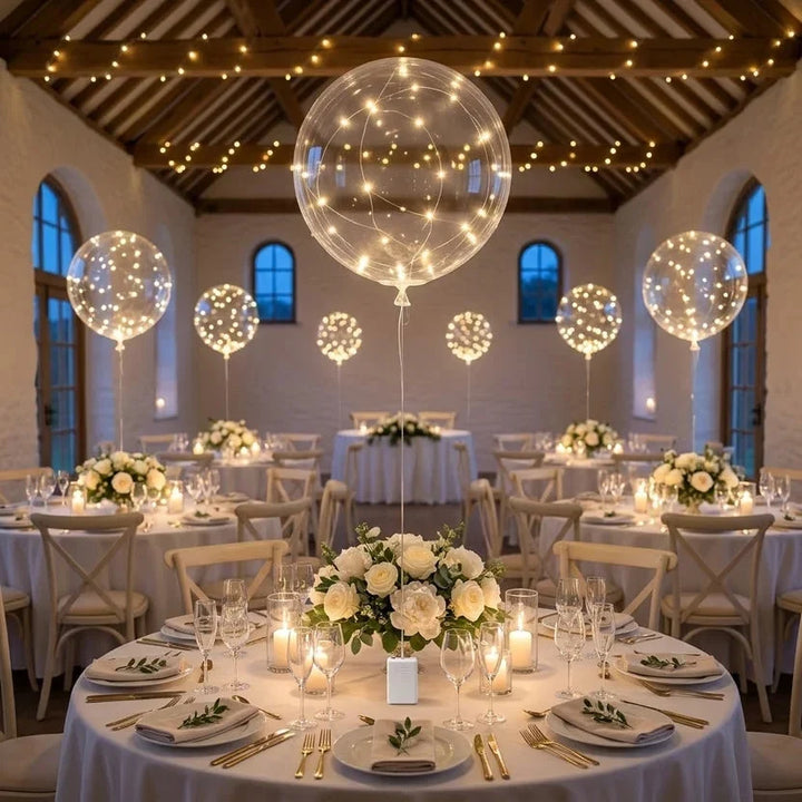 Lichtgevende ballonnen boven ronde tafels met witte bloemstukken in een feestzaal met lichtslingers 5