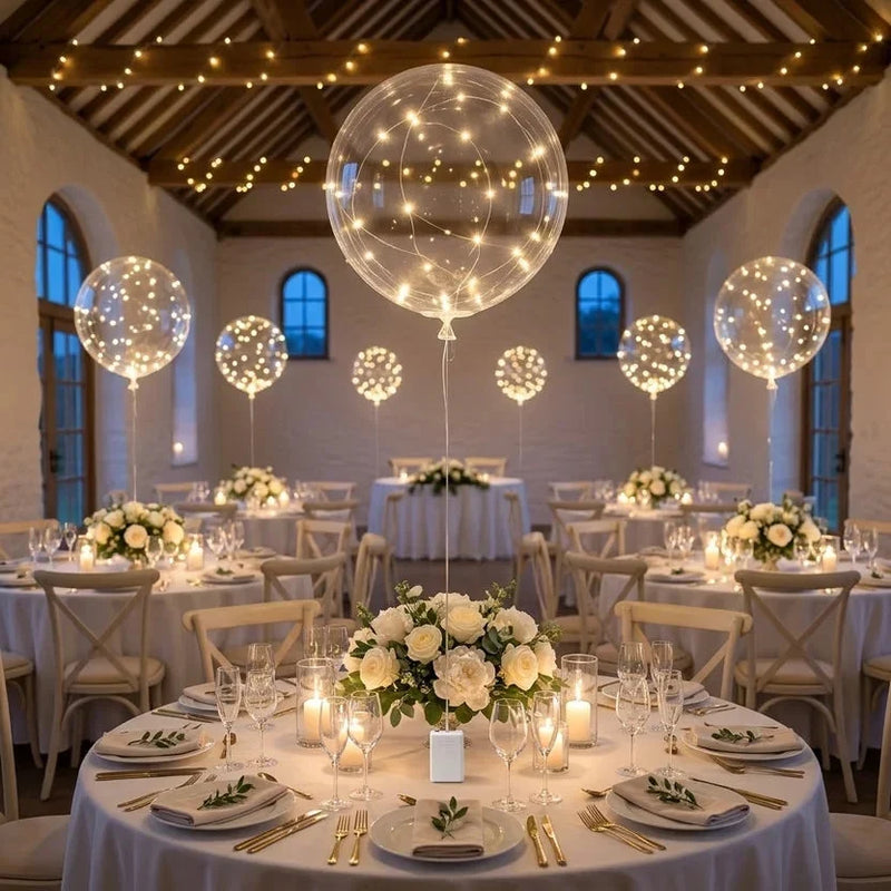 Lichtgevende ballonnen boven ronde tafels met witte bloemstukken in een feestzaal met lichtslingers 5