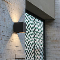 Detail van een zwarte wandlamp op een buitenmuur van natuursteen, met lichtbundels omhoog en omlaag naast een patroonscherm. 11