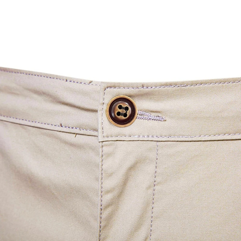 Close-up van de bruine knoop en het knoopsgat aan de tailleband van de beige short. 5