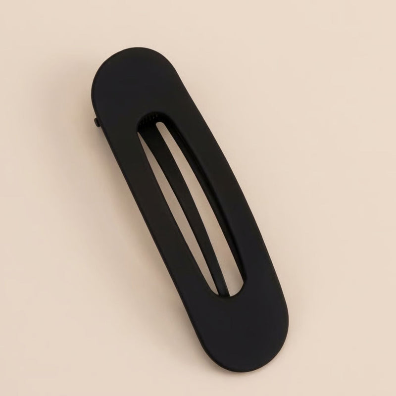 Zwarte matte platte haarclip met sleuf in het midden, liggend op een beige ondergrond 5