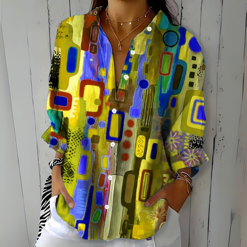 Model draagt de blouse in geel, blauw en paars met abstract patroon, losvallend model met opgerolde mouwen. 5