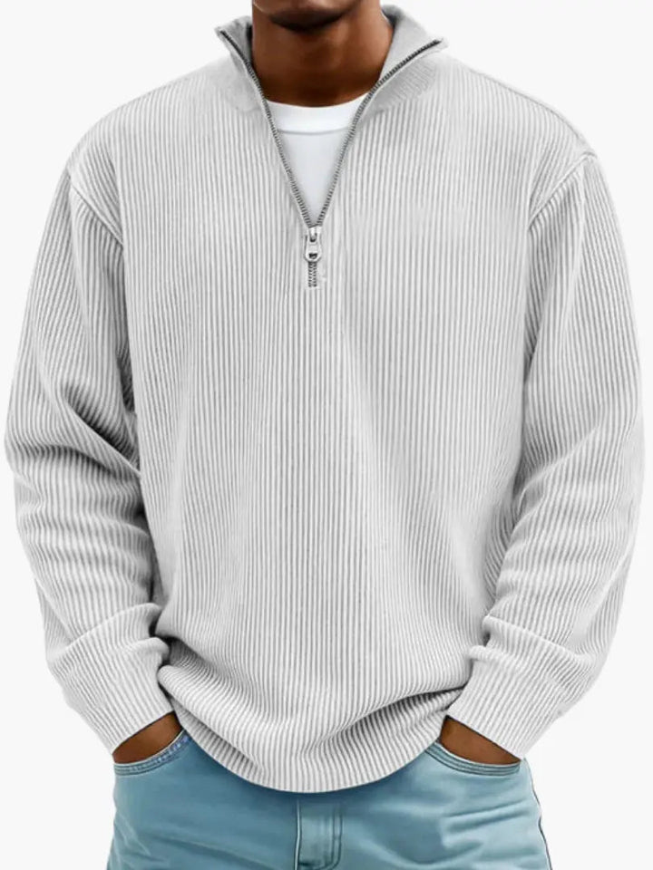 De geribbelde trui met kwartrits in lichtgrijs, gedragen over een wit shirt, met een model dat de handen in de broekzakken heeft. 6