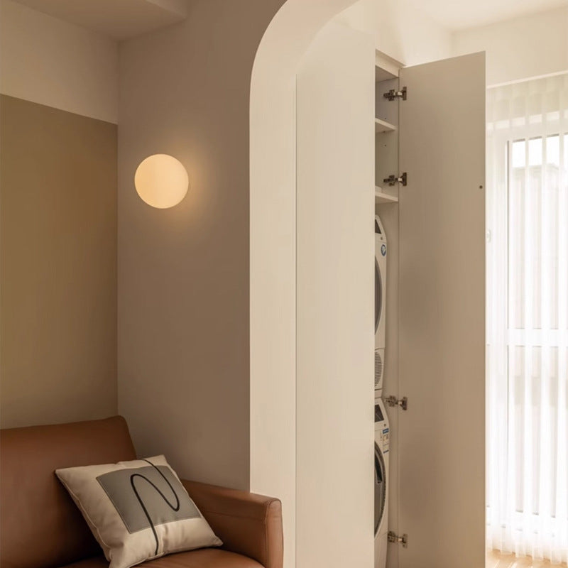 Kleine ronde wandlamp naast een boogvormige doorgang, boven een bank met kussen 4