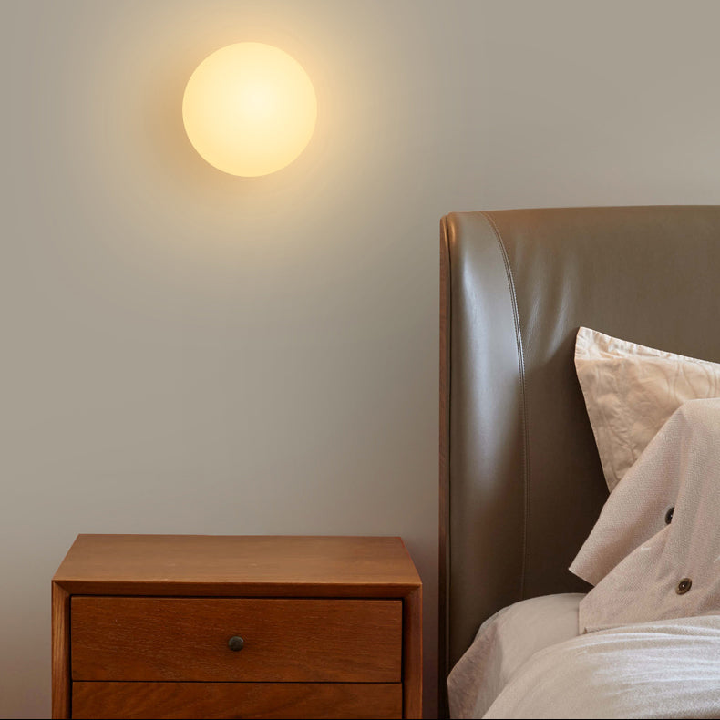 Lichtgevende bolvormige lamp aan de muur naast een houten nachtkastje en een leren bedhoofdeinde 2