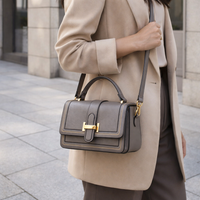Grijsbruine tas over de schouder gedragen door een model in beige blazer, met de band diagonaal over het lichaam. 4